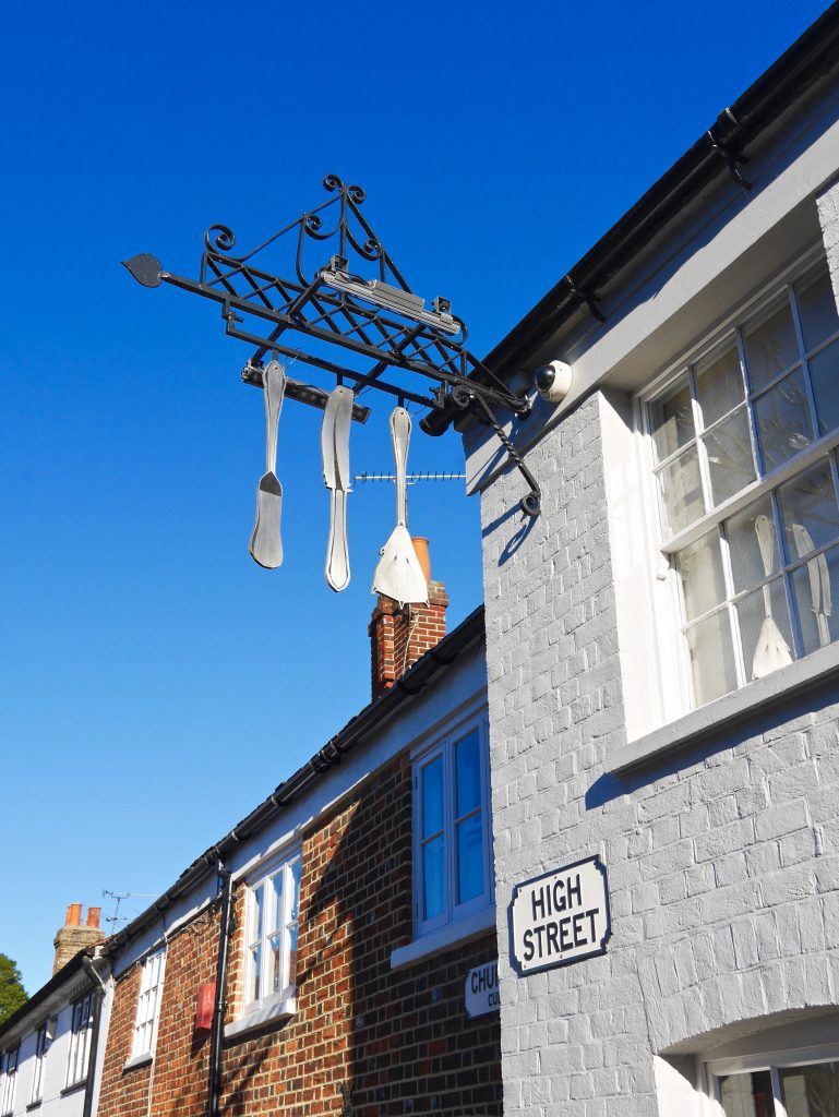 view of the hanging display of kitchen ware above the 'high street' street sign on. the side of the white bricked fat duck in bray