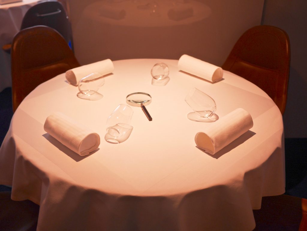 table set with rolled up towels, glasses on the side, a magnifying glass and hand stitched leather bucket chairs