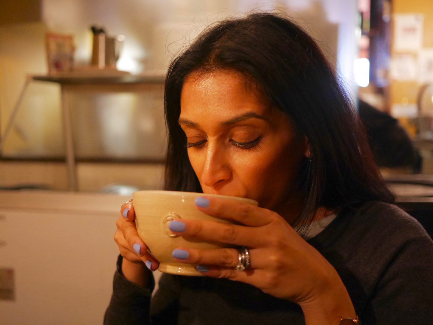sima drinking hot chocolate from a beige coloured cup with blue nails