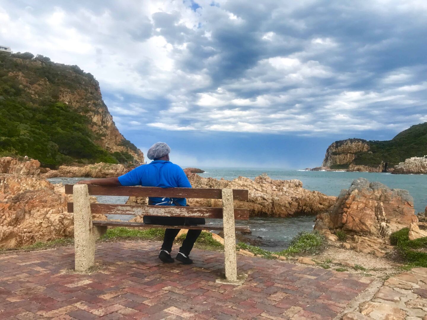 gentleman sat on a wooden bench wearing a blue t-shirt looking out at the lagoon