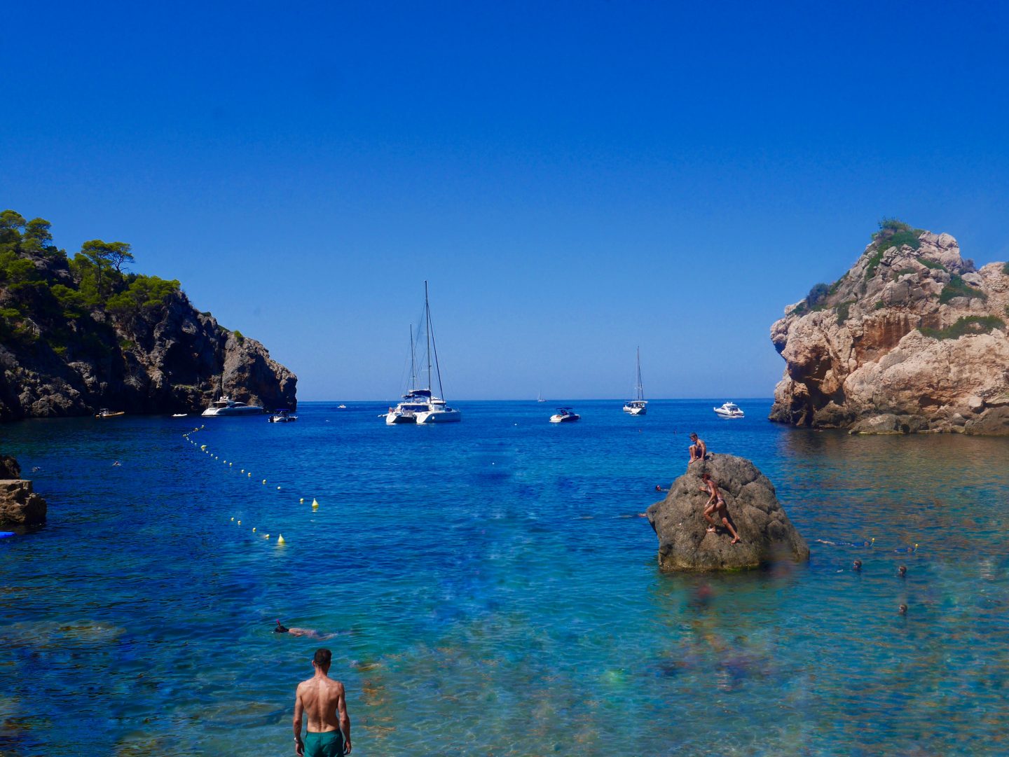looking out to see at Cala Deia with yachts and surrounded by rocks that people are climbing on