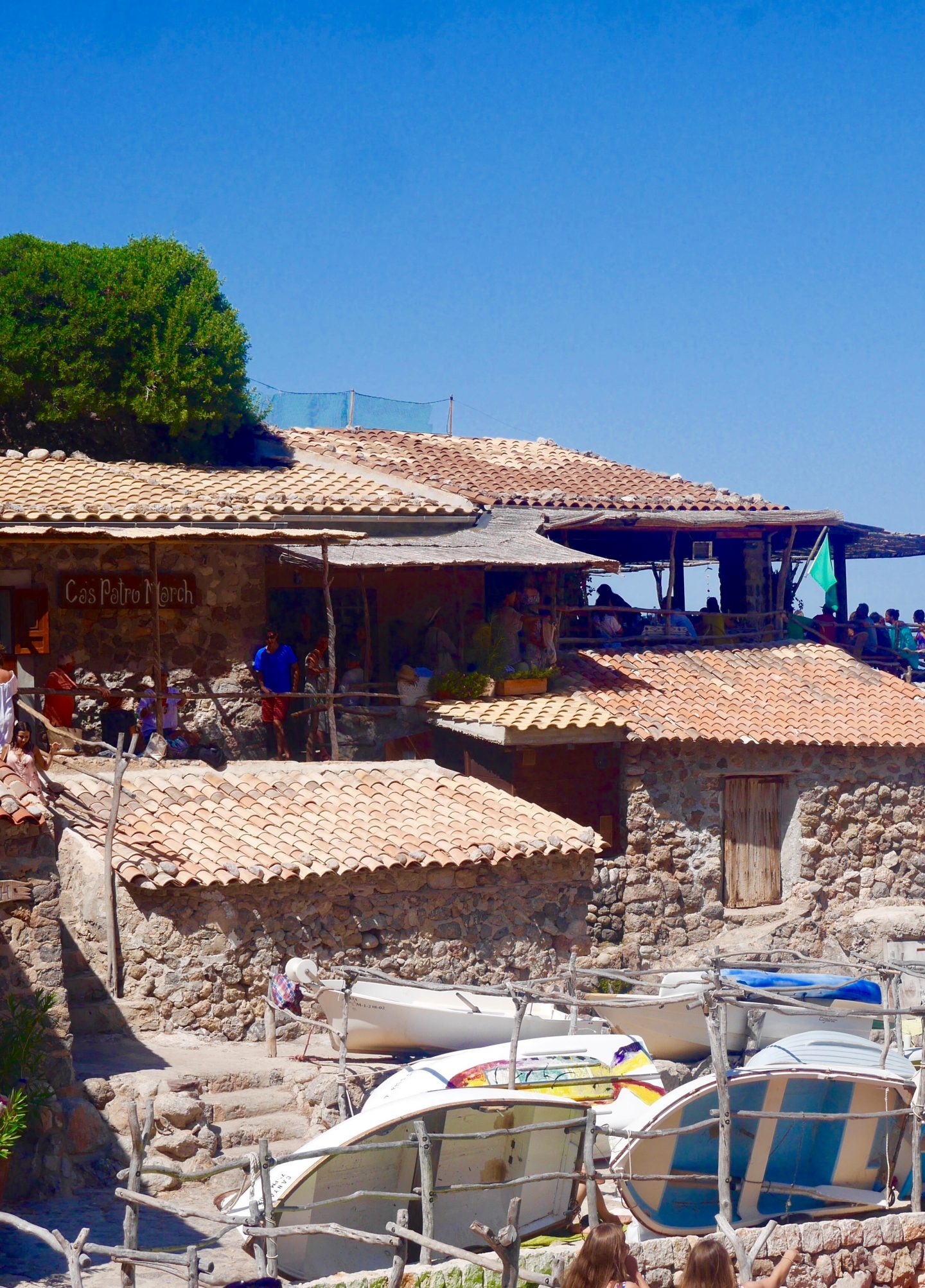 looking up to Ca's Patró March surrounded by tiled roof, old boats that are propped up against walls and fences and stone build sheds