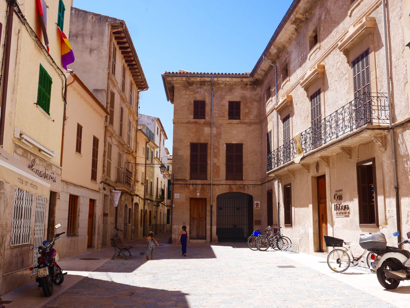 stone cobbled square with narrow street in the distance with bicycles and motorbikes parked up to the side
