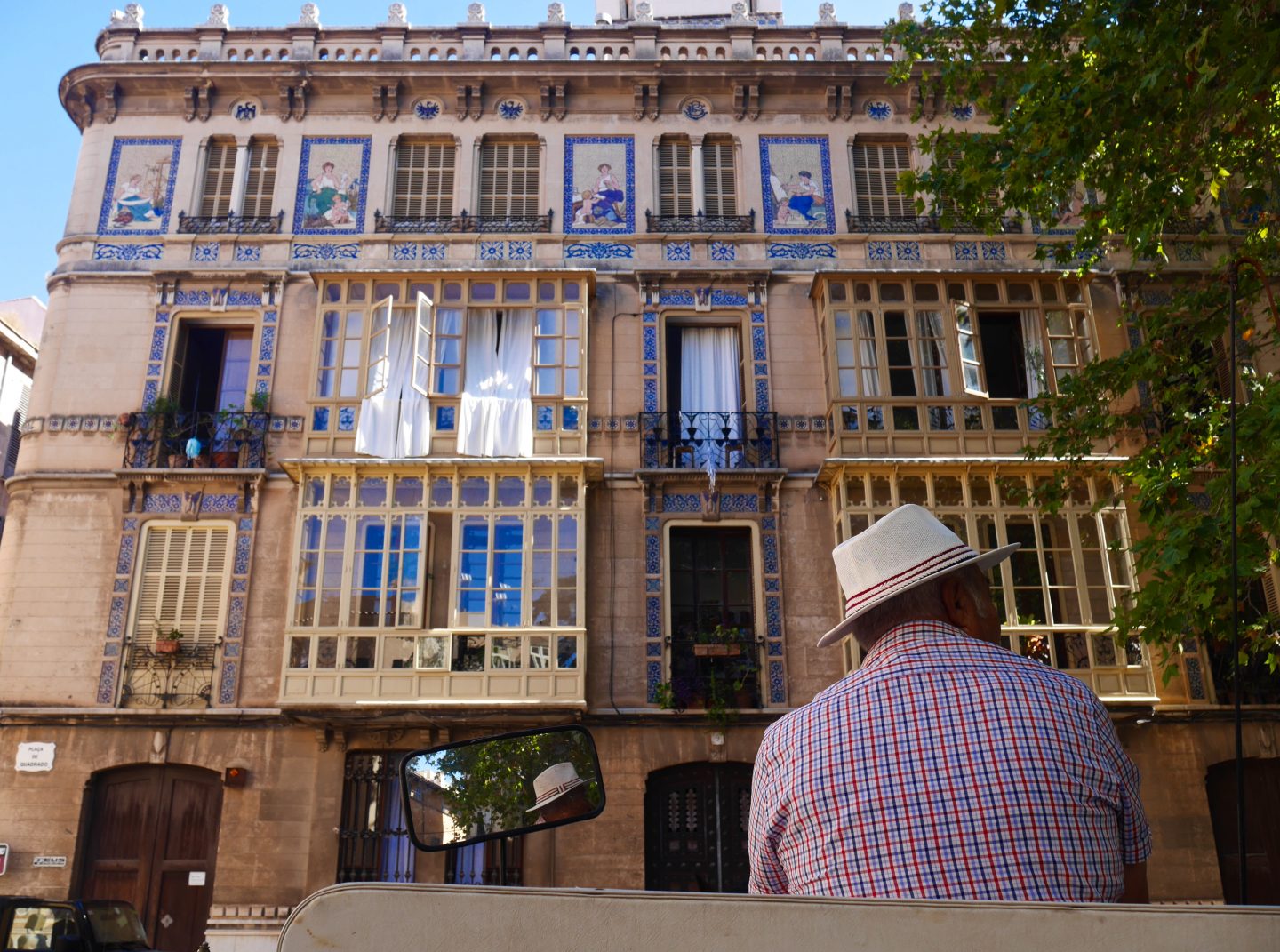 man facing away from camera in a red checked shirt and cream hat surrounded by incredible blue coloured architecture and windows in tall buildings