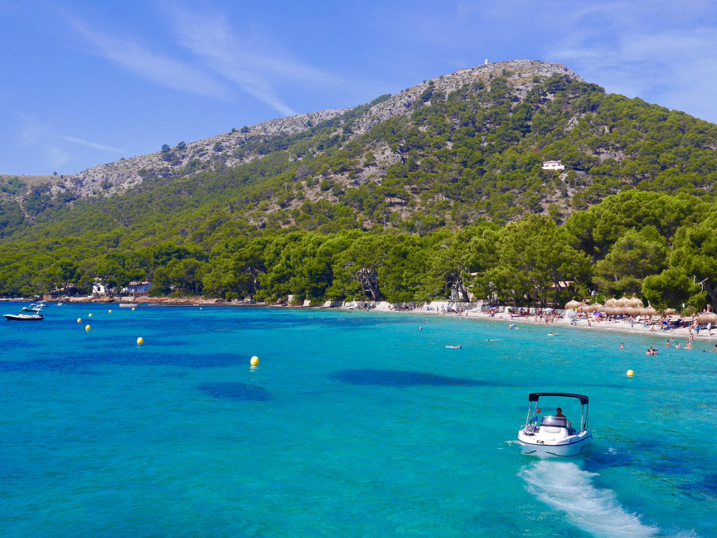 Cala Formentor beach in Mallorca with speed boat, bright blue sea surrounded by tall mountain covered in greenery