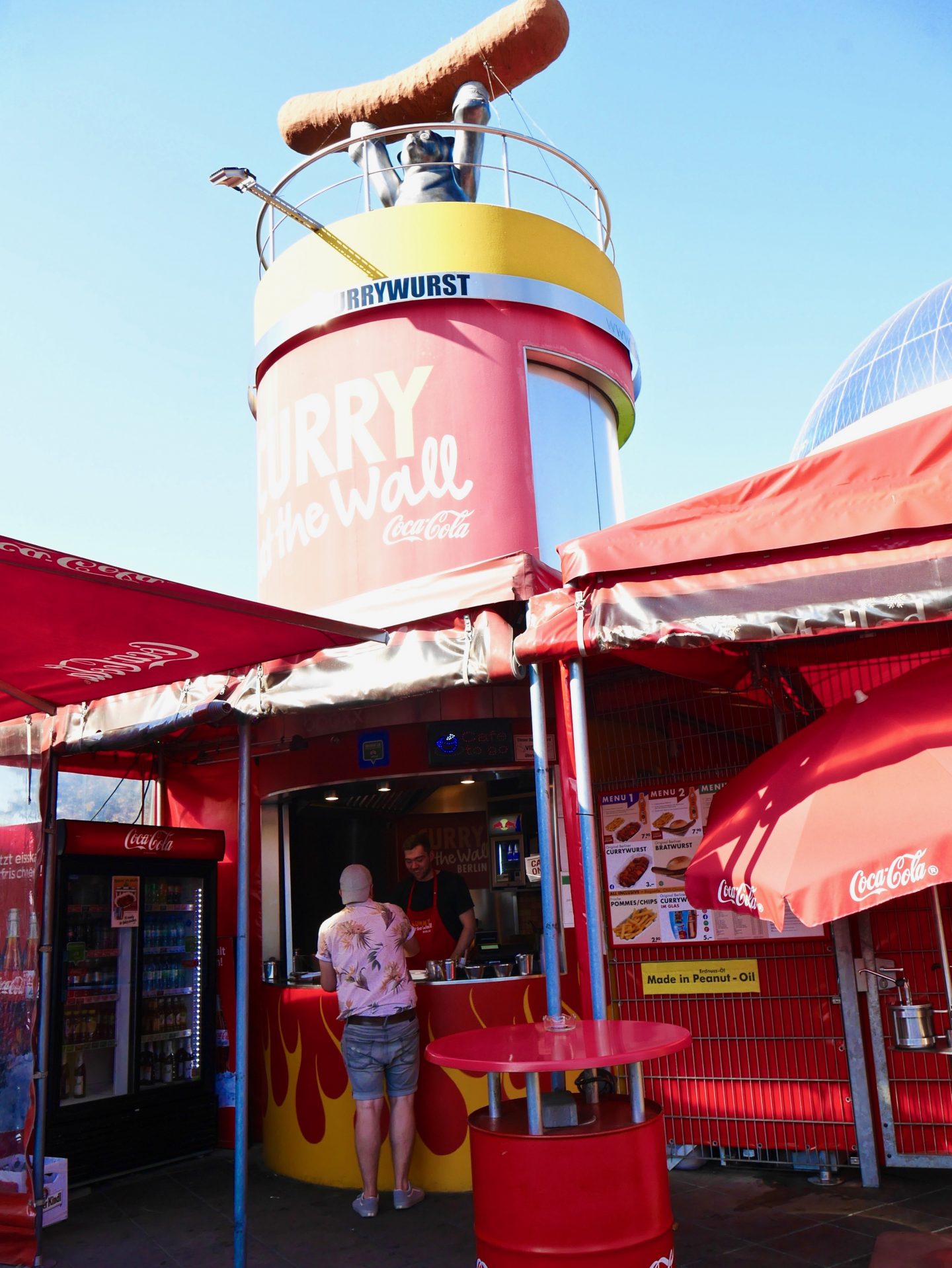 outside the curry at the wall. fast food with coca-cola branding colours and name and a sausage on the top of a tall tower