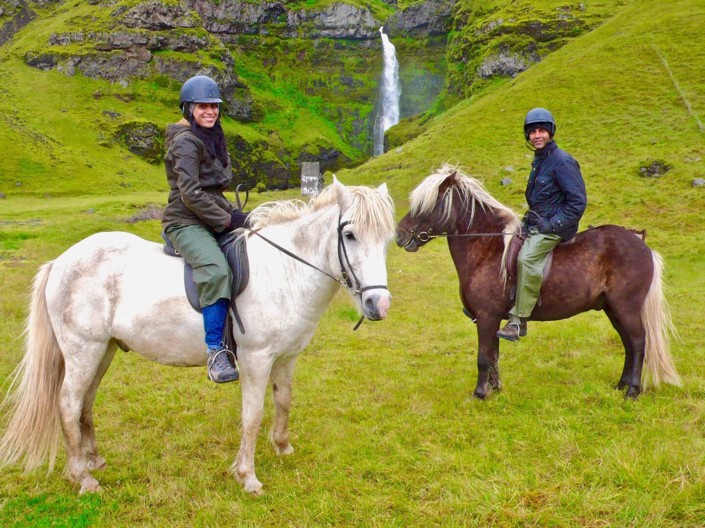 view of sima and husband on horses in Iceland with a waterfall in the background