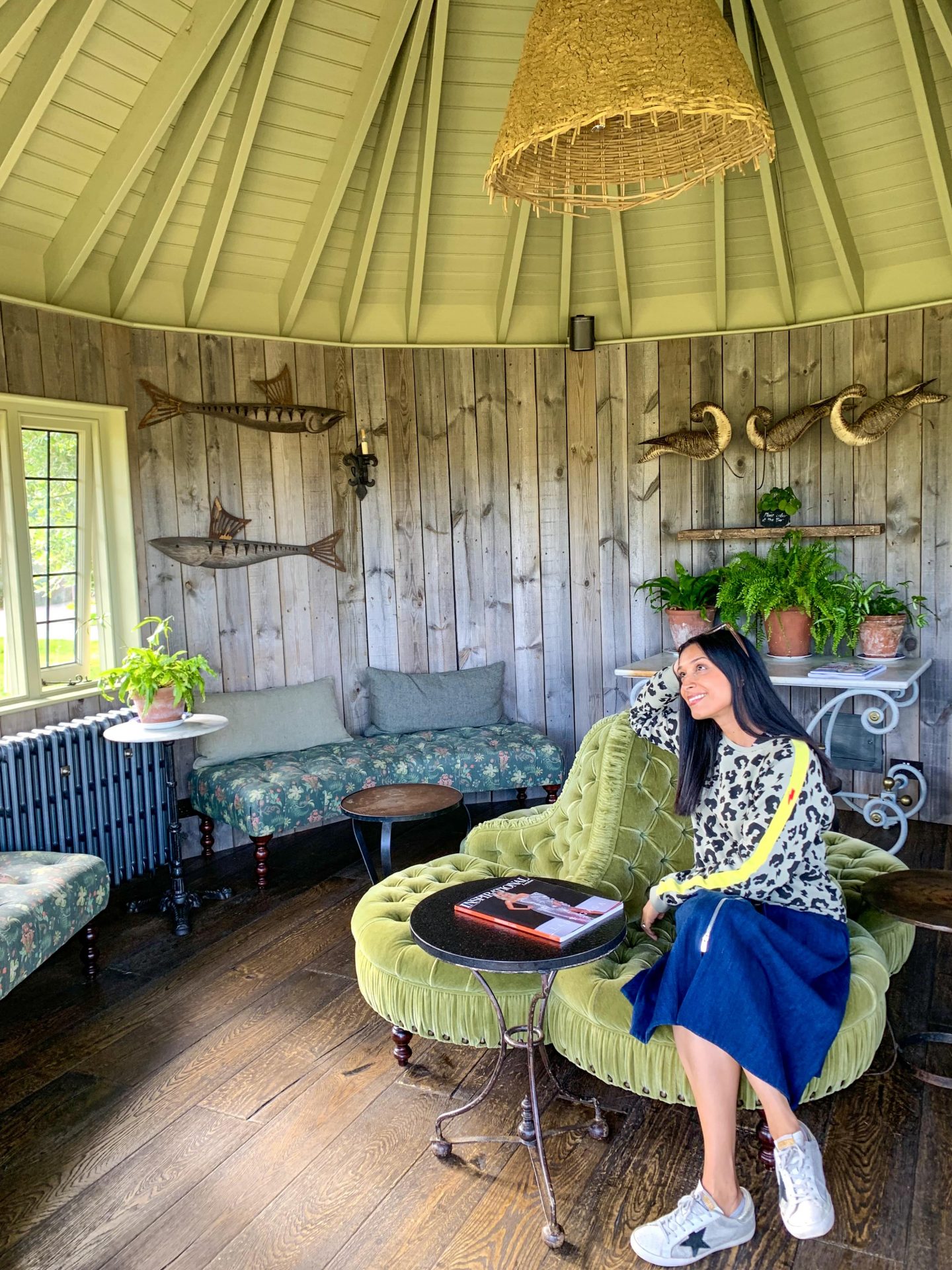 Sima inside the Roundhouse wooden house sat on green velvet chair admiring the decor, greenery and fish ornaments on the wall
