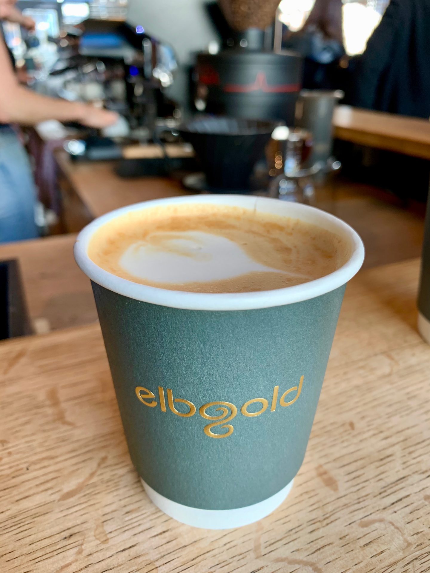picture of a green coffee cup on oak bar with a milk pattern on the top of the coffee