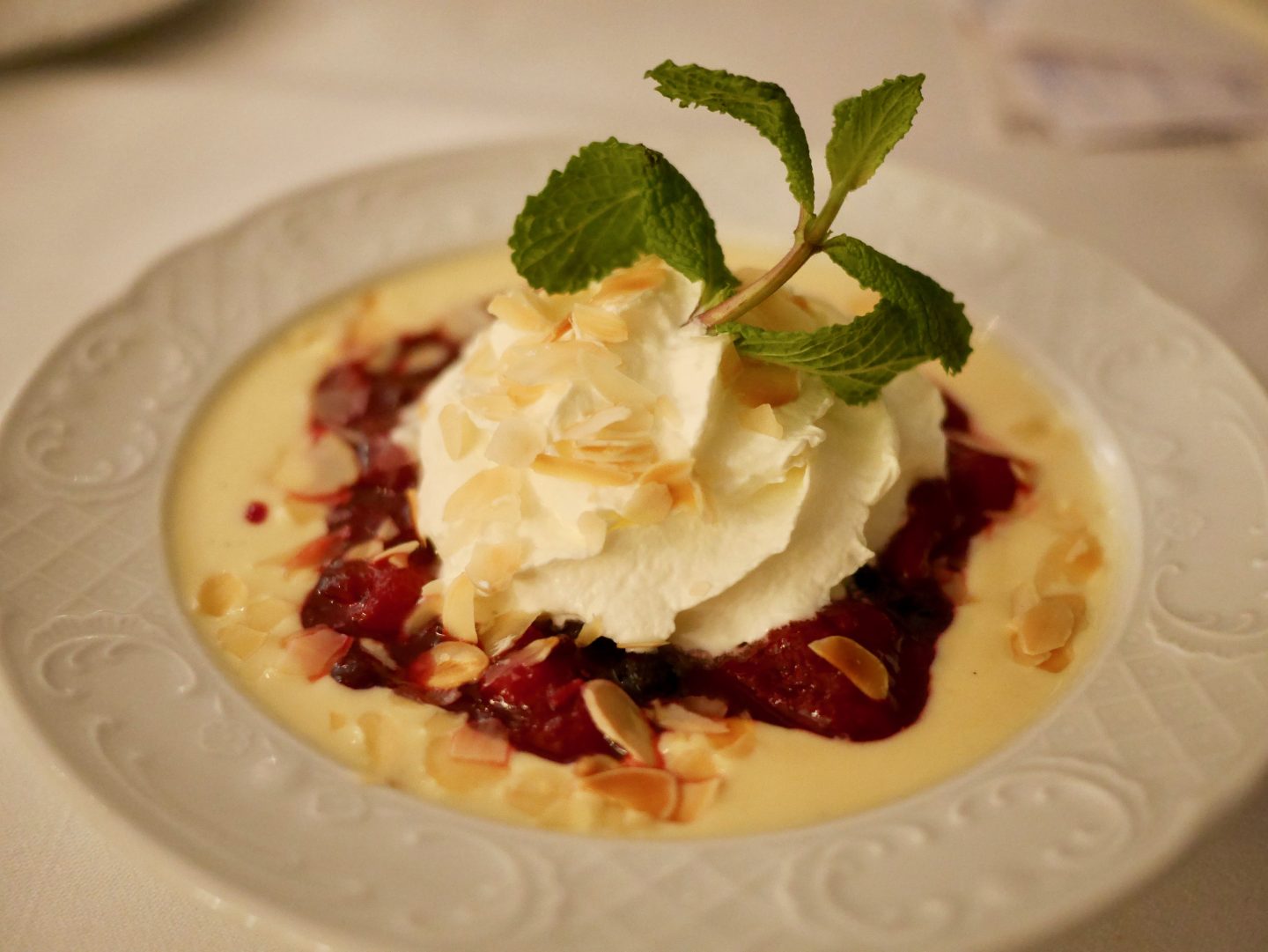 red berry compote served with vanilla custard, cream and sprinkled with almonds served on a white plate