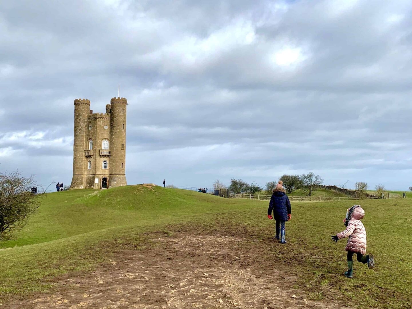 picture of two girls running on a field towards broadway tower in The Cotswolds