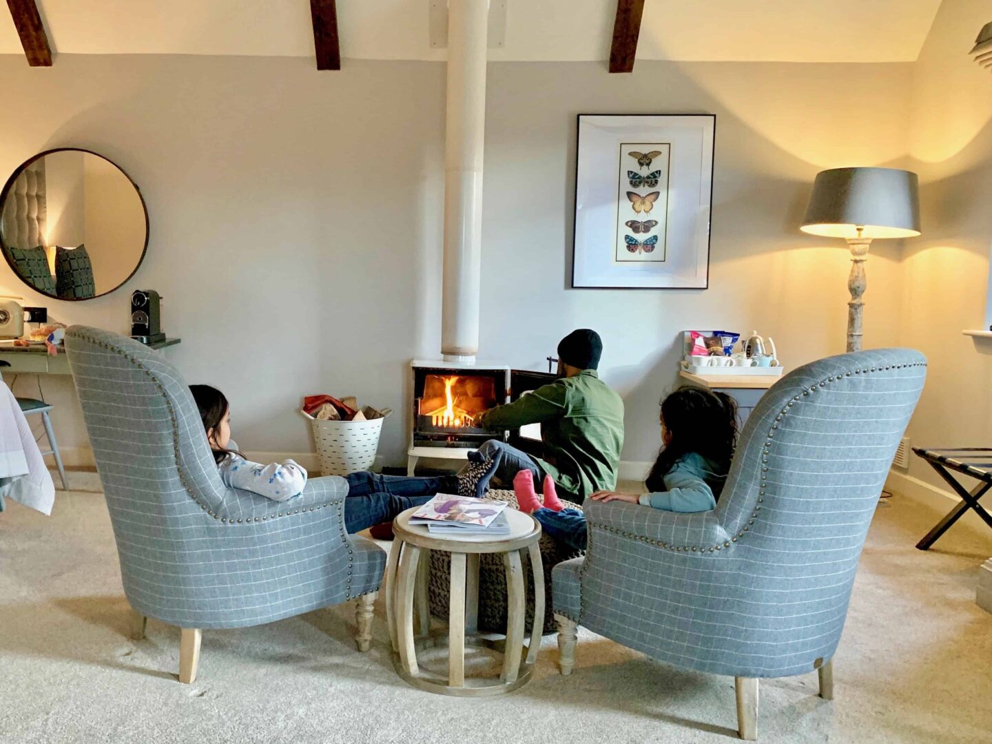 image of two chairs sat on by two girls and father in hat putting wood on the fire