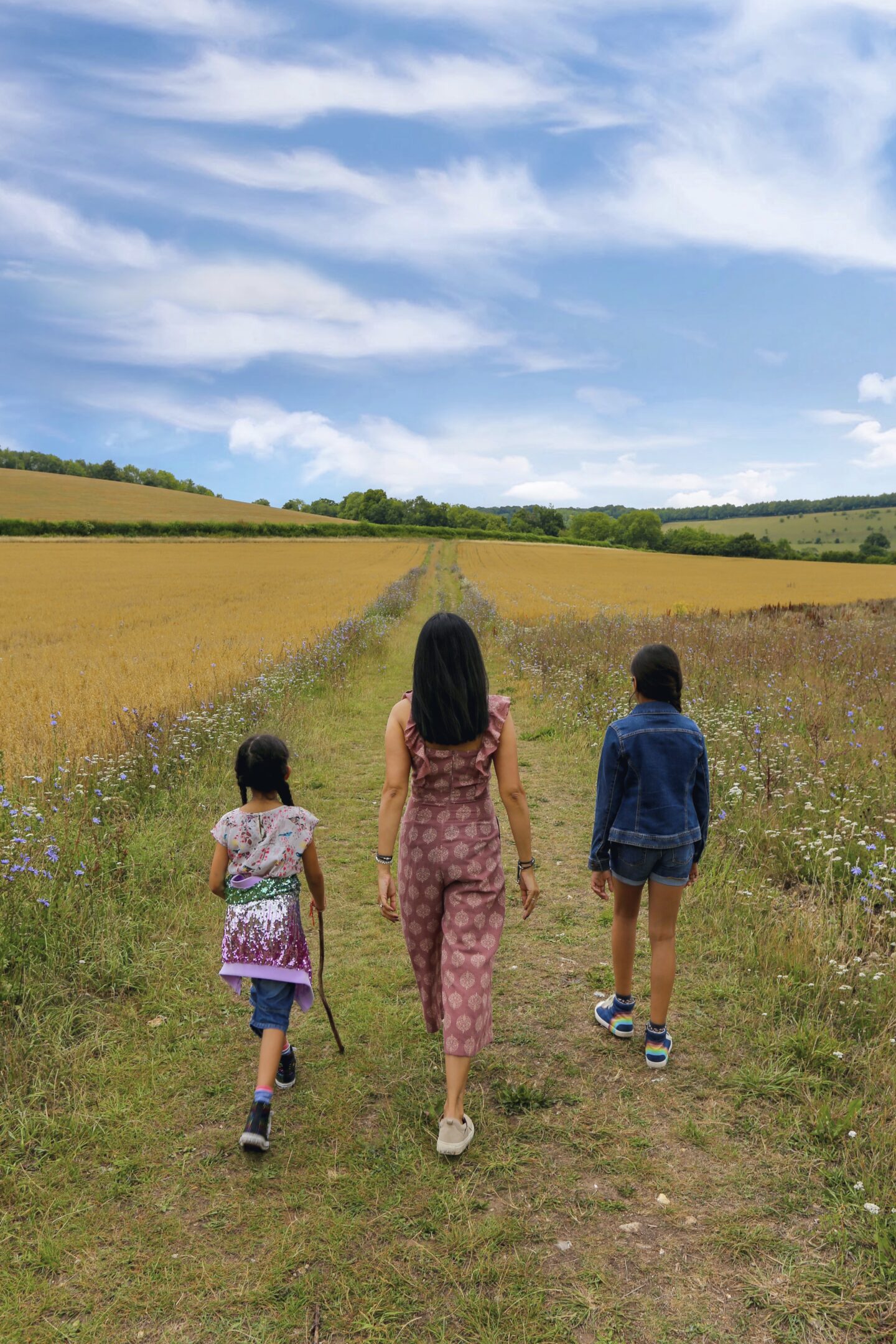 view of sima and her two girls walking away from the camera towards open fields