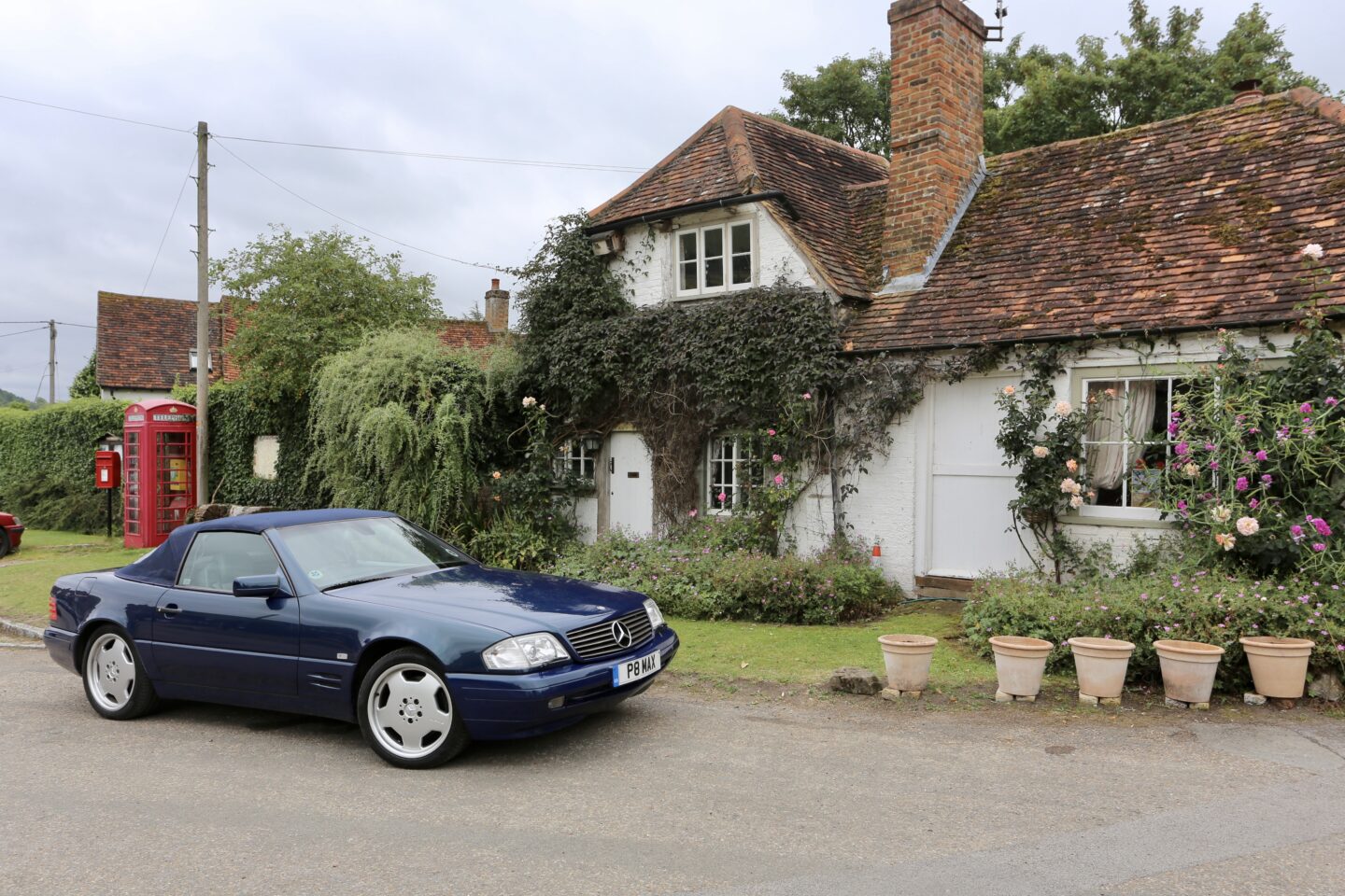 view of a Mercedes convertible in front of a small cottage covered with trees