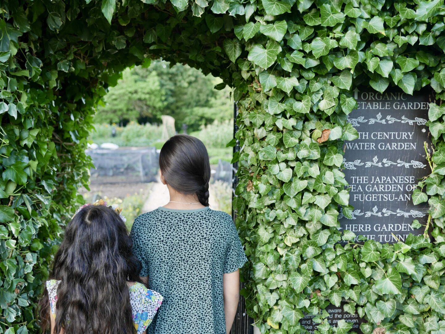 view of simas daughter stood in a arch way of foliage and a slate sign