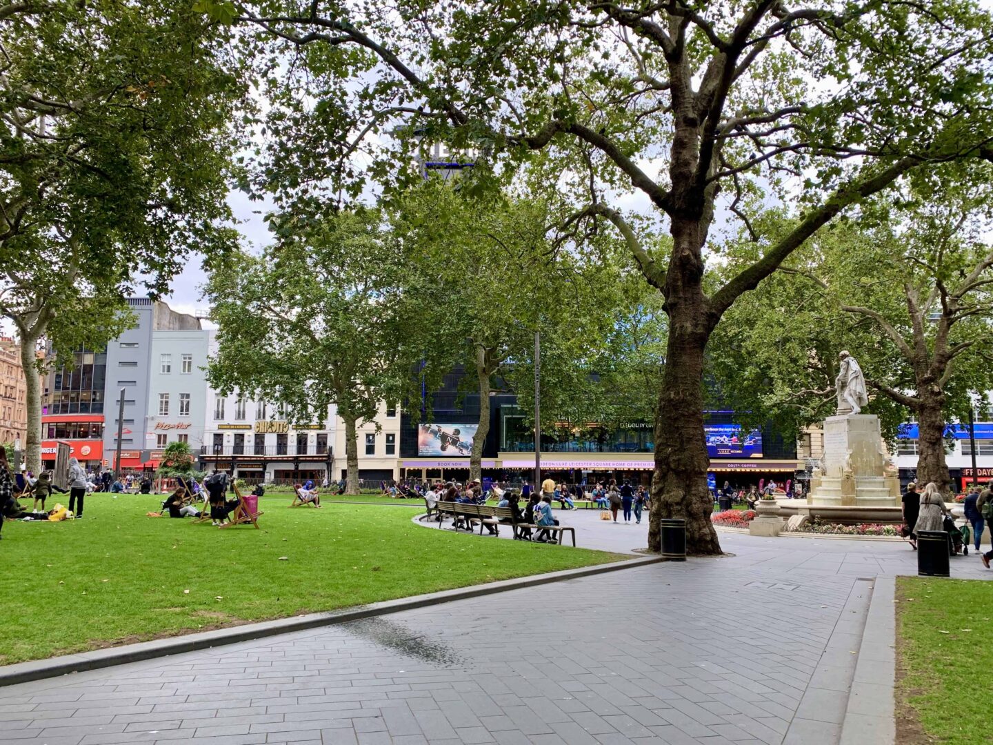 view of Leicester Square with monument and people sat on grass