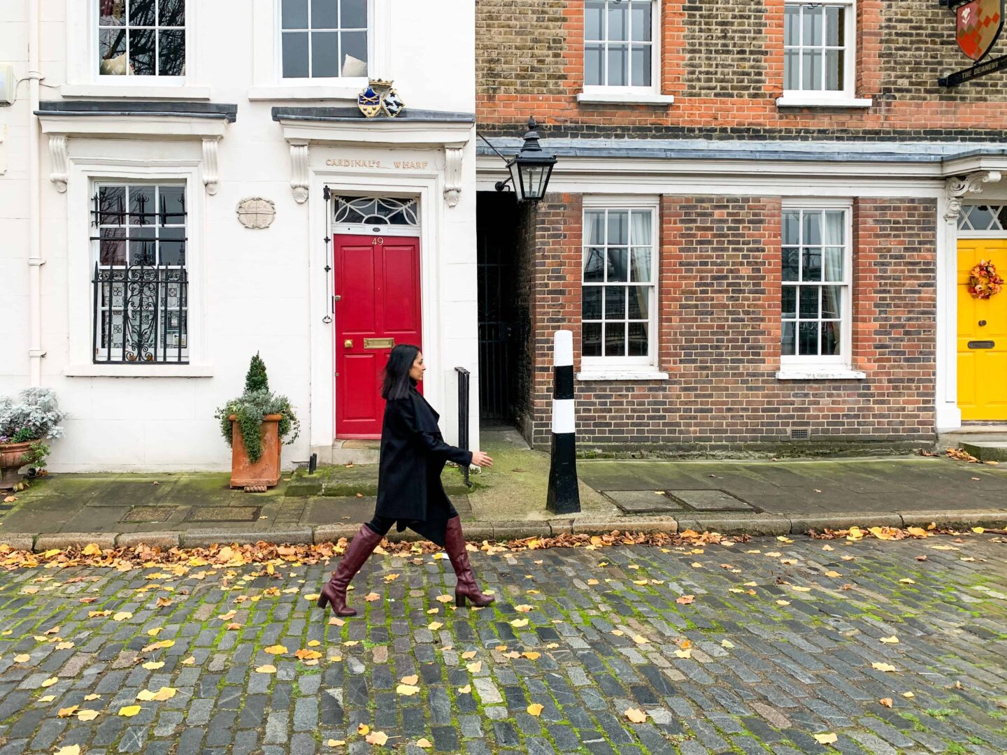 sima walking down a cobbled London street in front. of houses with yellow and red doors